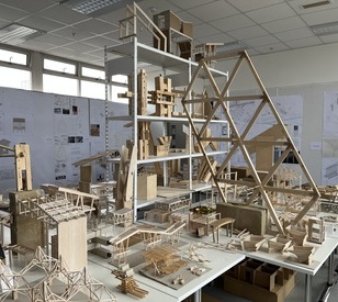 Architectural studio with wooden models and sketches displayed on walls. The models vary in size and complexity, conveying creativity and innovation.