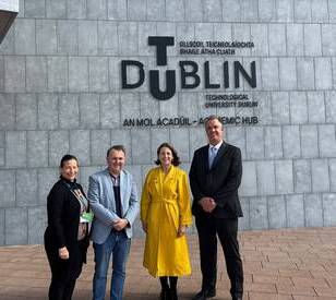 Four people stand in front of a wall with the large text “DUBLIN Technological University Dublin Academic Hub” and its Irish translation.