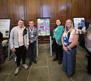 Four people standing in front of information display boards at an indoor event.